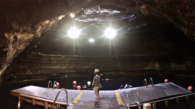 Homestead Crater. A large underground hot spring in Utah. A young boy stands on a dock above steaming water. He looks toward a hole in the ceiling of a cavern.
