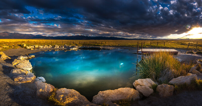 Meadow Hot Springs. A crystal clear pool with a small dock rests on a grassy cattle range at dusk. 