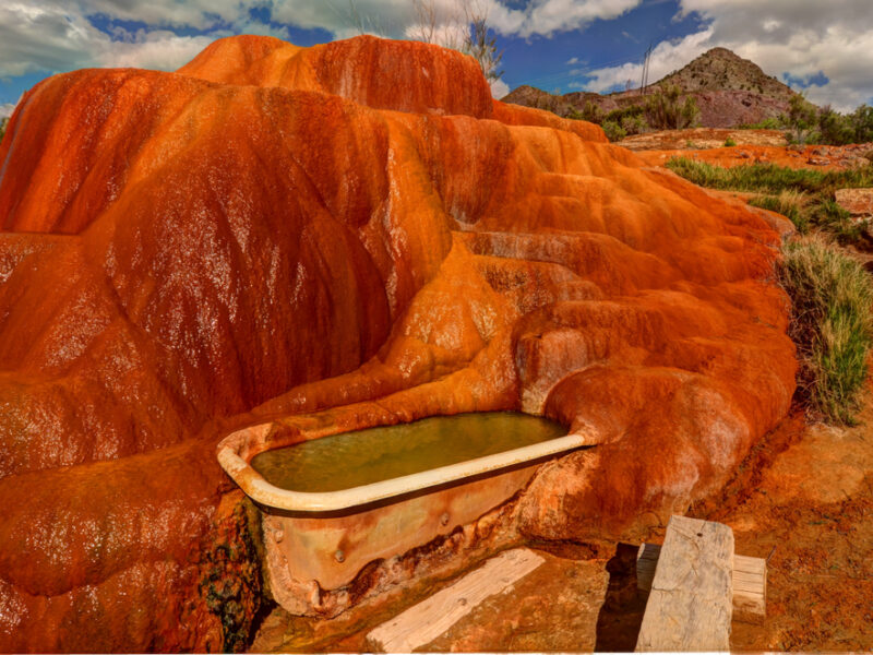 Mystic Hot Springs in Utah. A vintage tub filled with warm water sits against a red rock backdrop. 