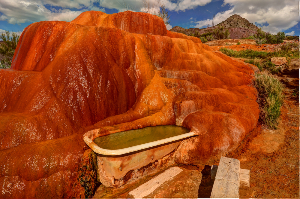 Mystic Hot Springs in Utah. A vintage tub filled with warm water sits against a red rock backdrop.