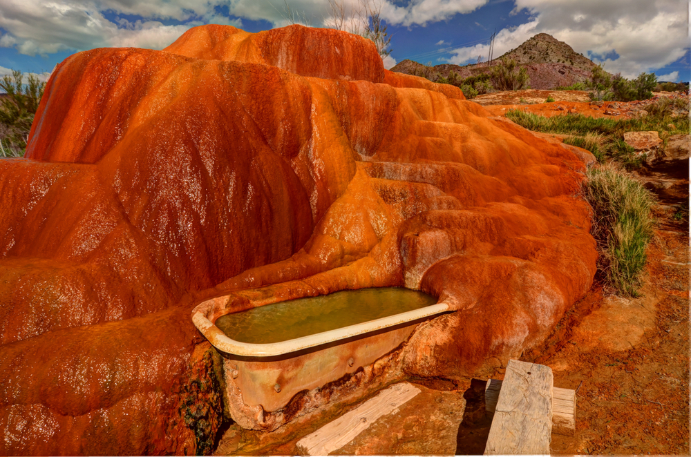 Mystic Hot Springs in Utah. A vintage tub filled with warm water sits against a red rock backdrop.