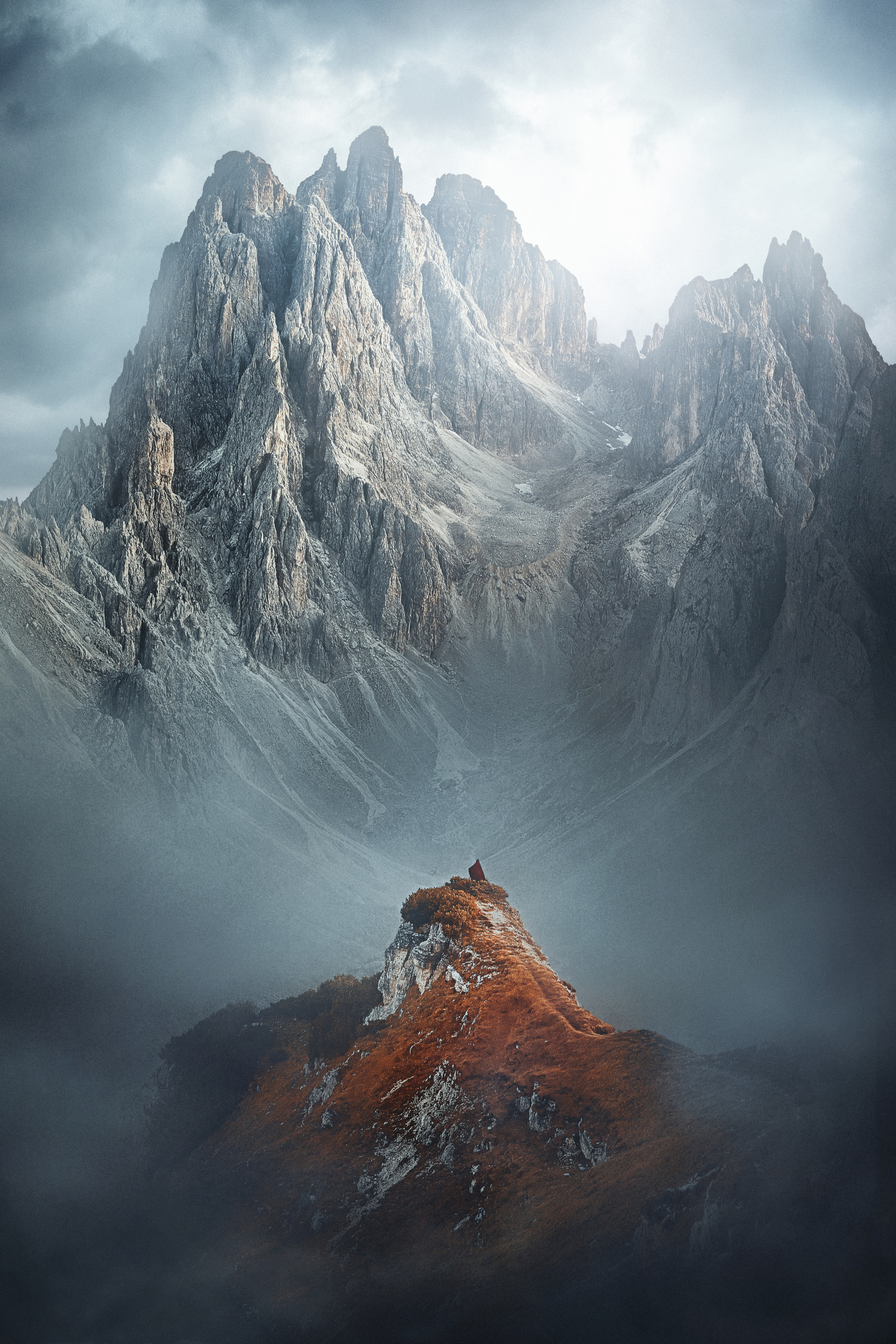 Wide angle photo of a woman standing in red cape with mountains in background at Cima Cadin one of the hidden gems in Italy.