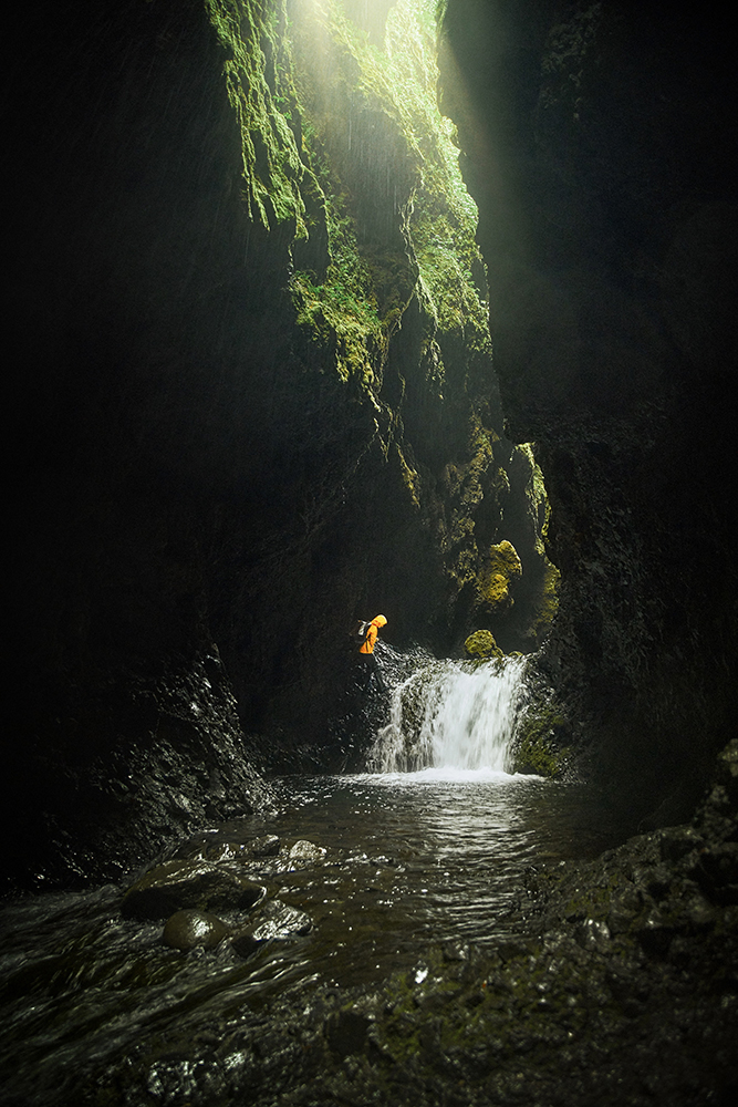 Woman in yellow jacket hiking near waterfall in ravine in Iceland