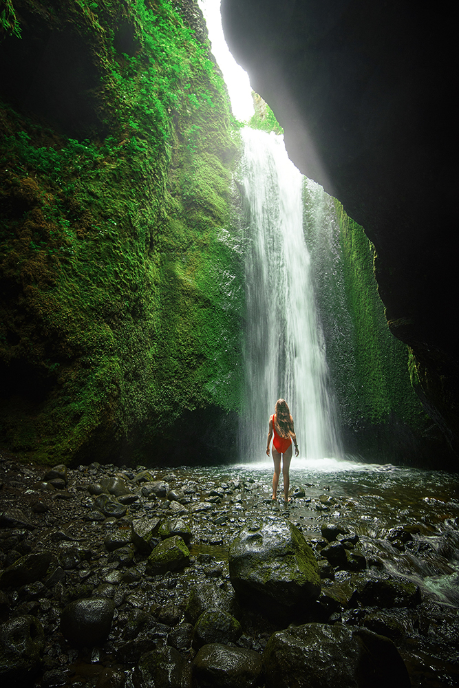 Woman in red bathing suit standing in front of Nauthusagil Waterfall in Iceland