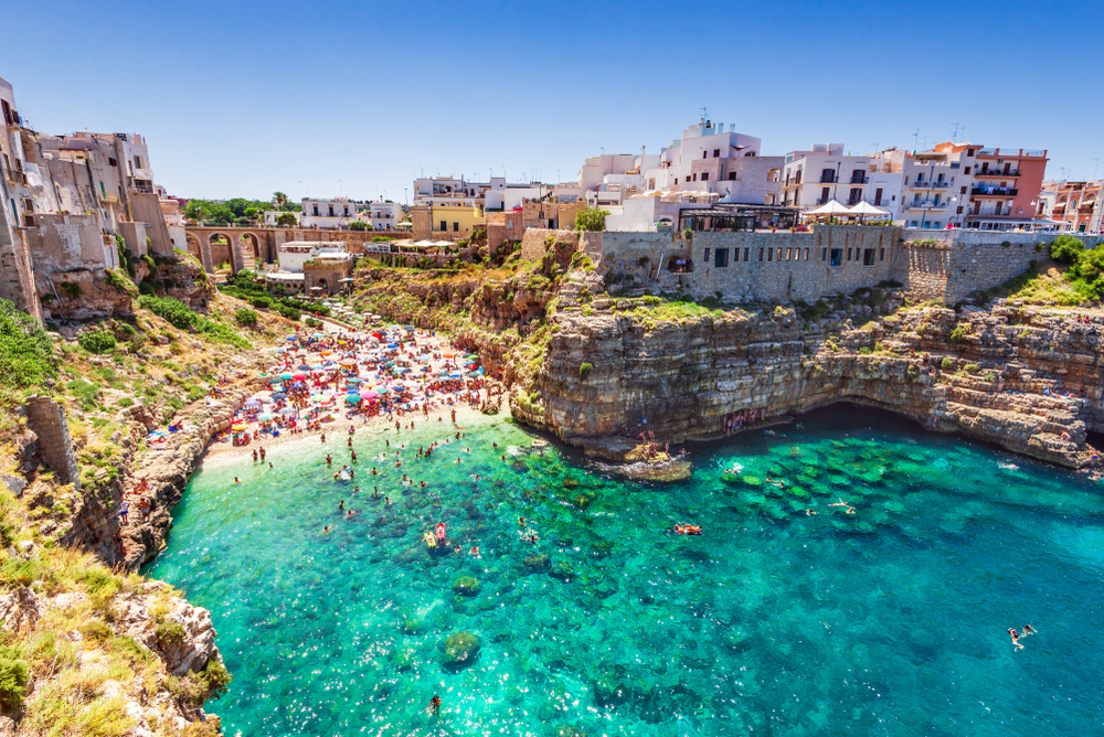 Aerial view of vibrant turquoise waters leading to a beautiful beach and one of the best beach towns in Italy, Polignano a Mare. 