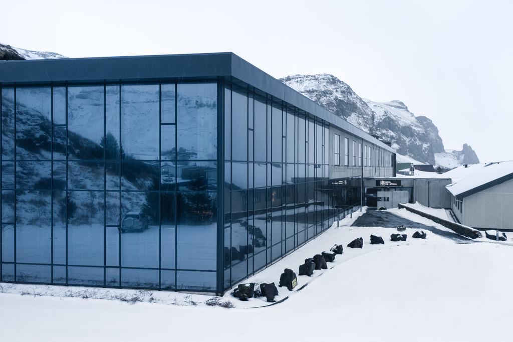 Photo of Hotel Vík í Mýrdal with gray blue glass windowed walls set against a snowy mountain backdrop and foreground.