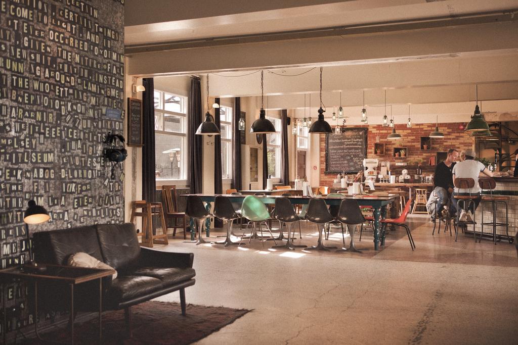 Photo of the communal space inside of Kex Hostel located in Reykjavik Iceland. Lunchroom style seating the main focus with a small seating area in the foreground.