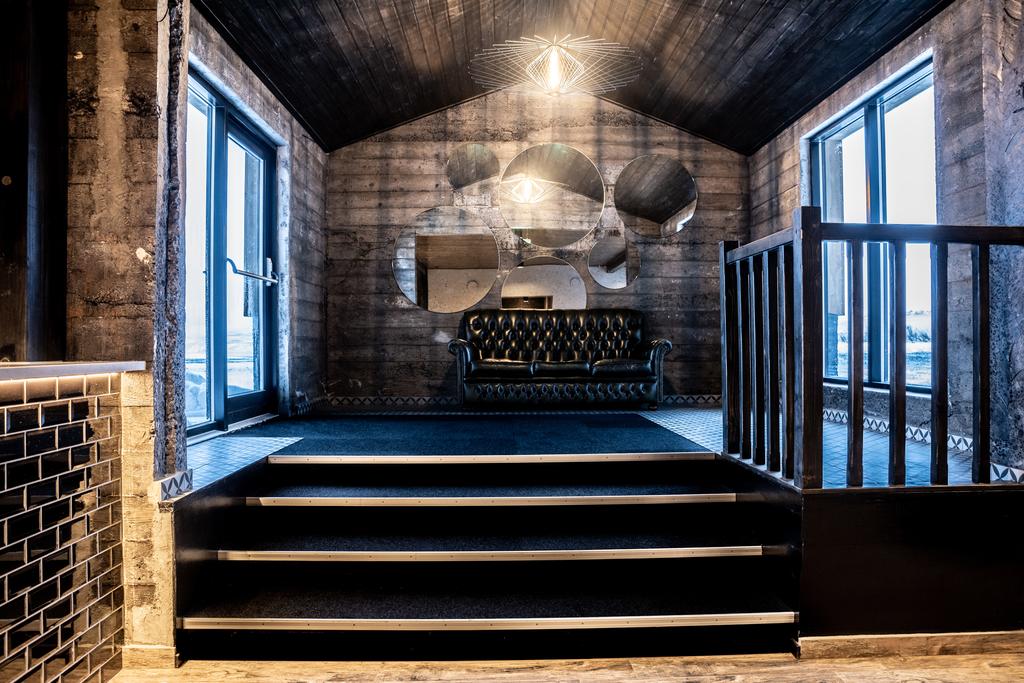 Photo of a seating area in The Barn which is located in Vik Iceland. Dark wood walls and flooring are seen with a small stair case leading up to a small couch. 