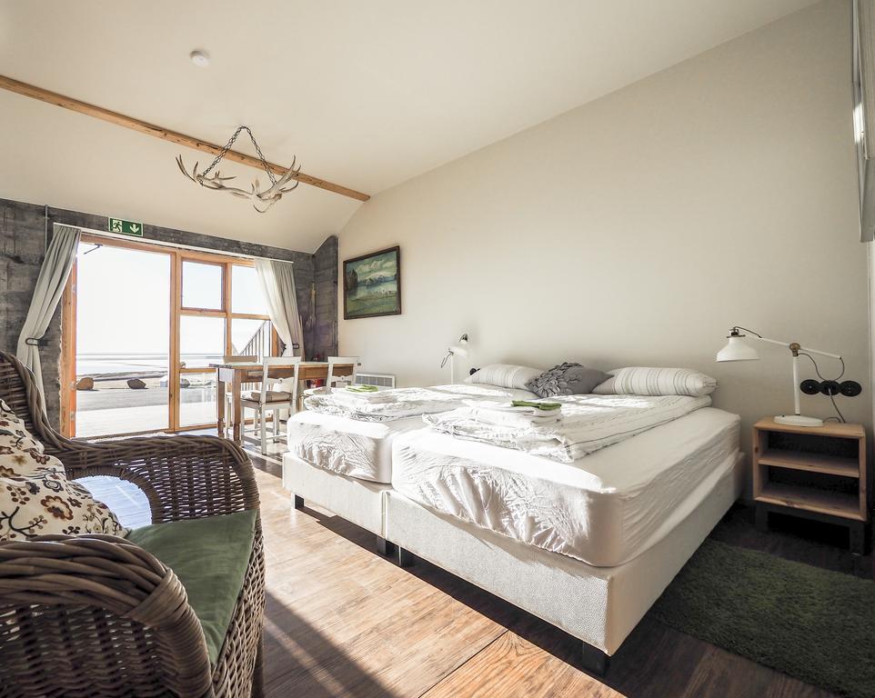 Photo of a guest room at The Garage Apartments located in Vik Iceland. A crisp and light decor is seen in this well appointed room. Bed linens are neatly folded and placed at the foot of the beds. A wicker chair is seen in the foreground.