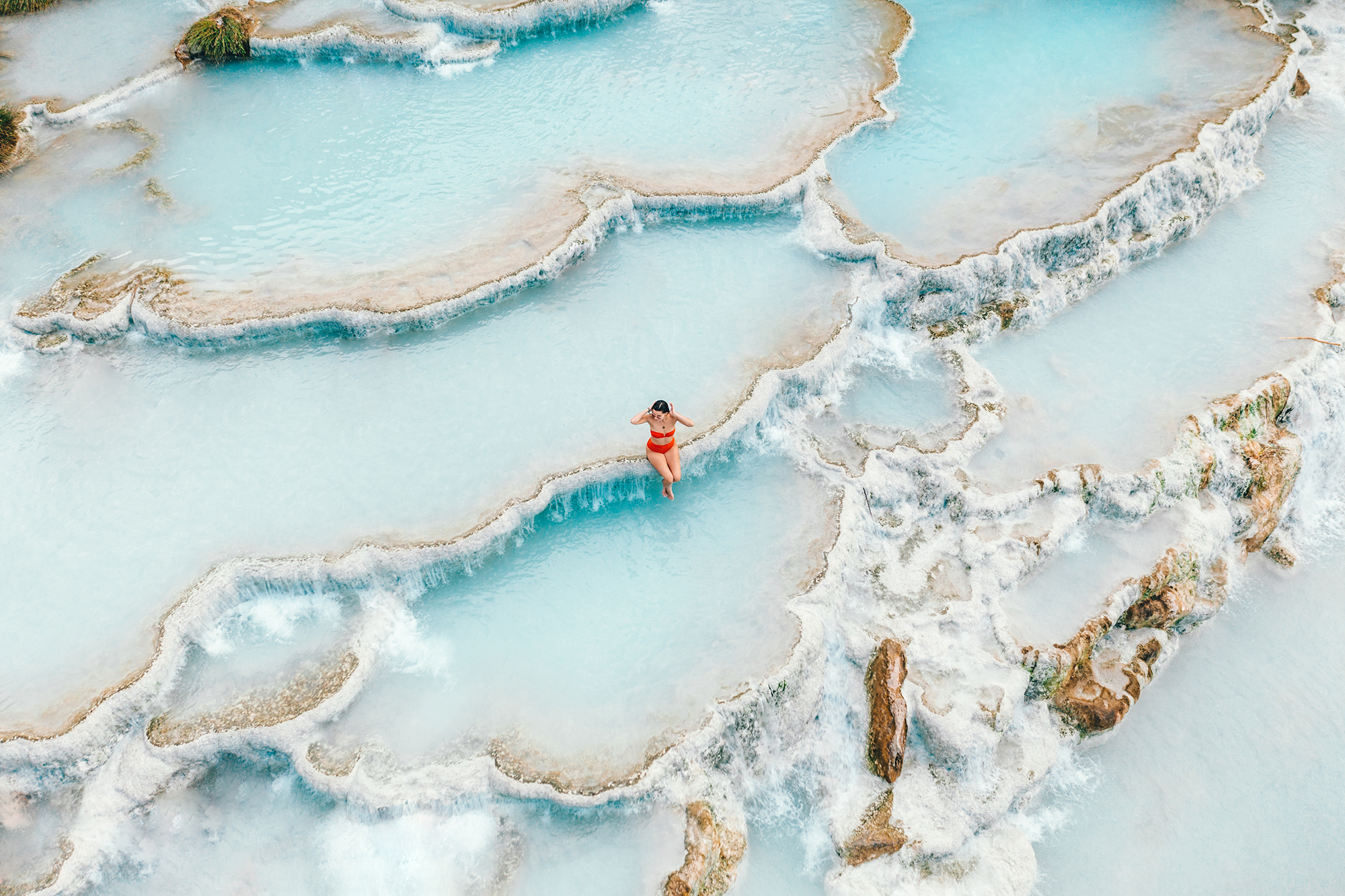 woman in red bathing suit sitting on edge of Saturina Hot Springs with blue water