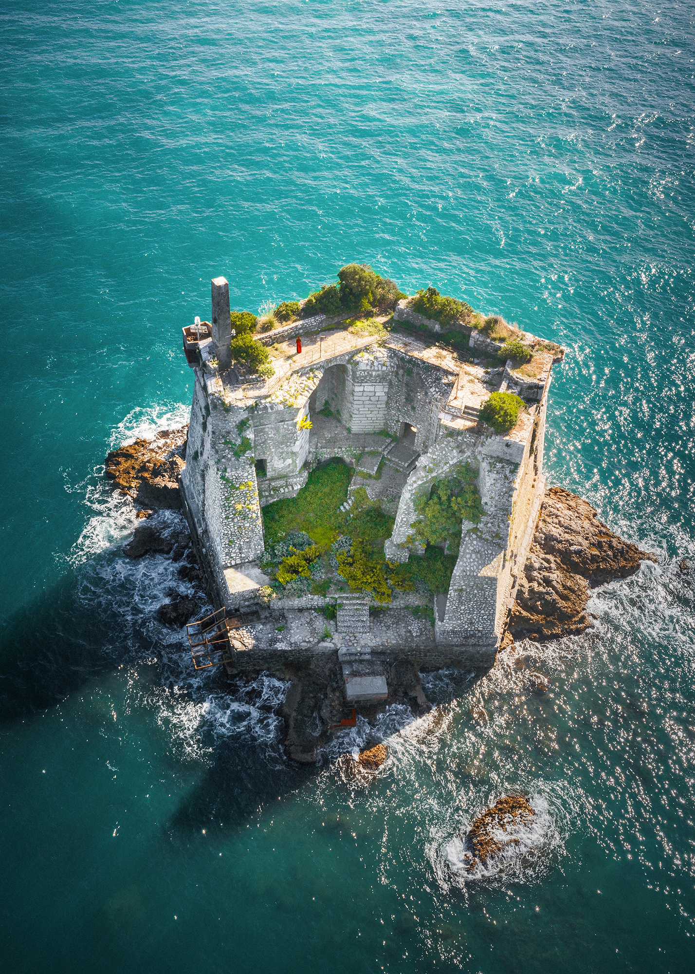 A drone photo of old Genoa fortress Scola Tower surrounded by green water.