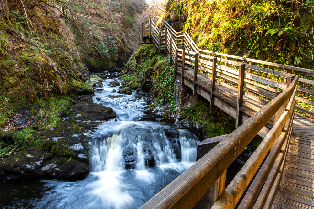Hiking through the glens of Antrim is one of the many things to do in northern ireland that hikers love. The photos shows one of the waterfalls you can see on the hike with a wooden walkway off to the side.