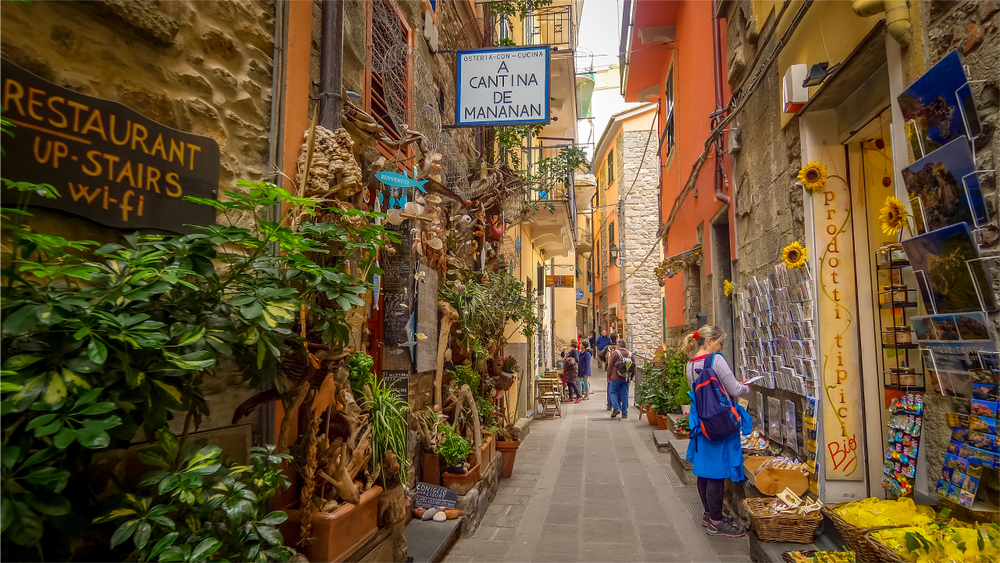 A narrow alley with shops in the Cinque Terre village of Corniglia . You can see shops and a few people in the article.