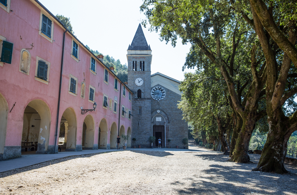 Photos of Sanctuary of Nostra Signora di Soviore. You can see the road, the trees and a pink building. It is one of the things to do in Cinque Terre. 