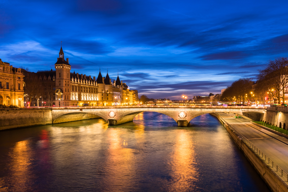 View of a bridge over the river with buildings lit up at dusk.