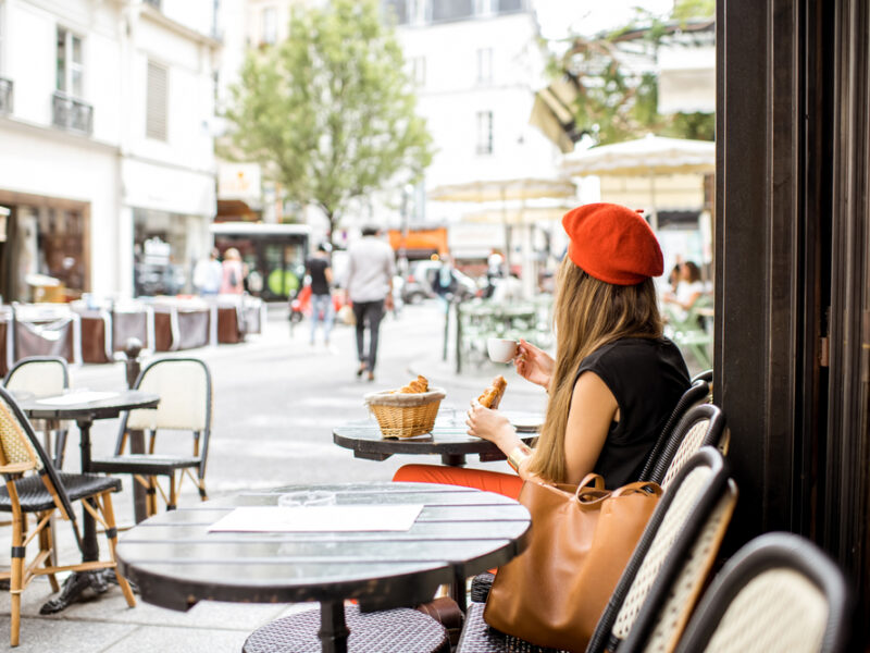A young stylish woman in a red beret samples a baguette at a Parisian cafe. 