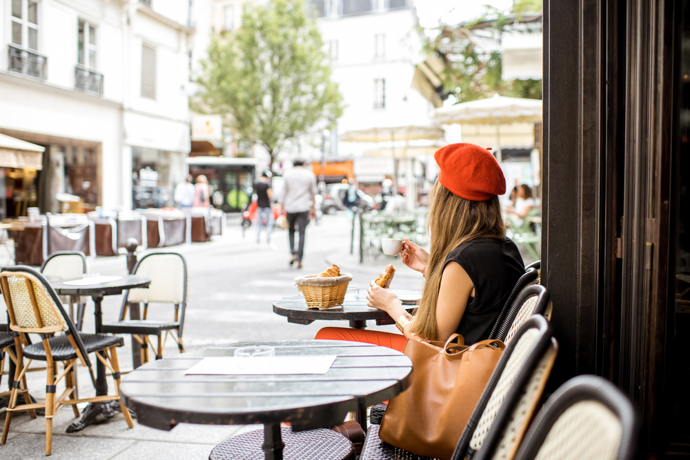 A young stylish woman in a red beret samples a baguette at a Parisian cafe.