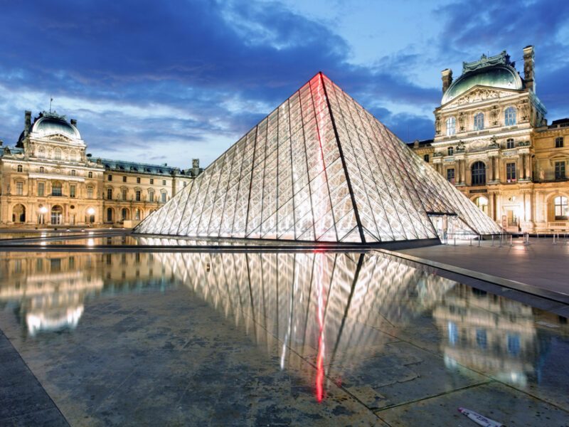 A view of the Louvre Museum in Paris at night all lit up from the inside. 