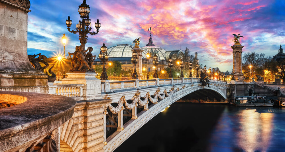 A twilight view of the seine in Paris with streetlamps lining a decorative bridge.