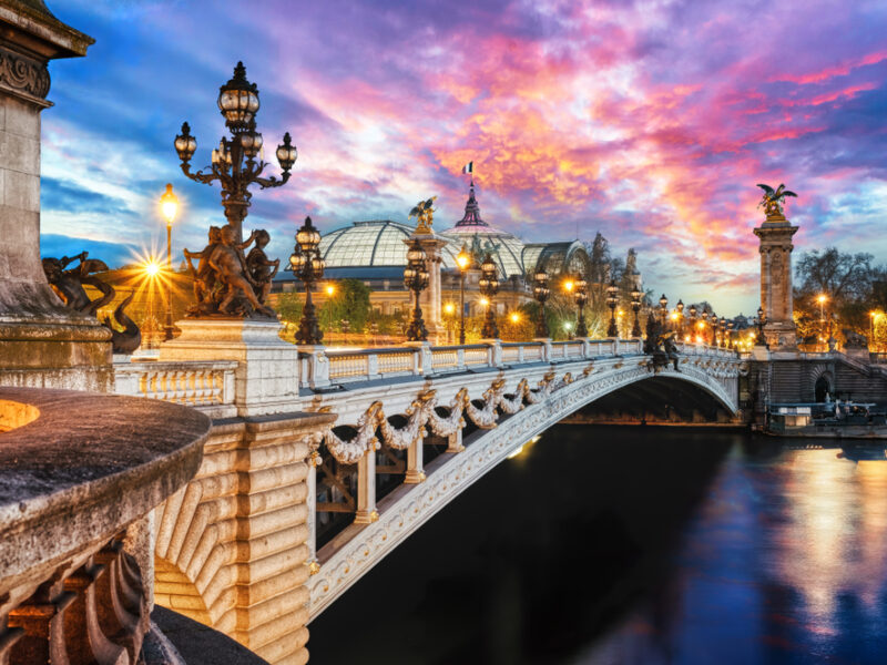 A twilight view of the seine in Paris with streetlamps lining a decorative bridge. 