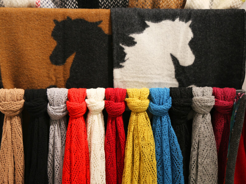 A selection of scarves, laid out by color. Two of the scarves depict a horse design. 
