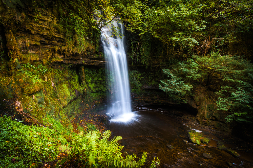 Glencar Waterfall flowing into a pool surrounded by greenery.