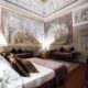 Photo of guest room at Hotel Burchianti in Florence Italy. Room is ornate a large bed with white linen sheets and plum and green velvet pillows. Plum velvet cushioned benches line the room. Large frescoes are on the walls and ceiling.