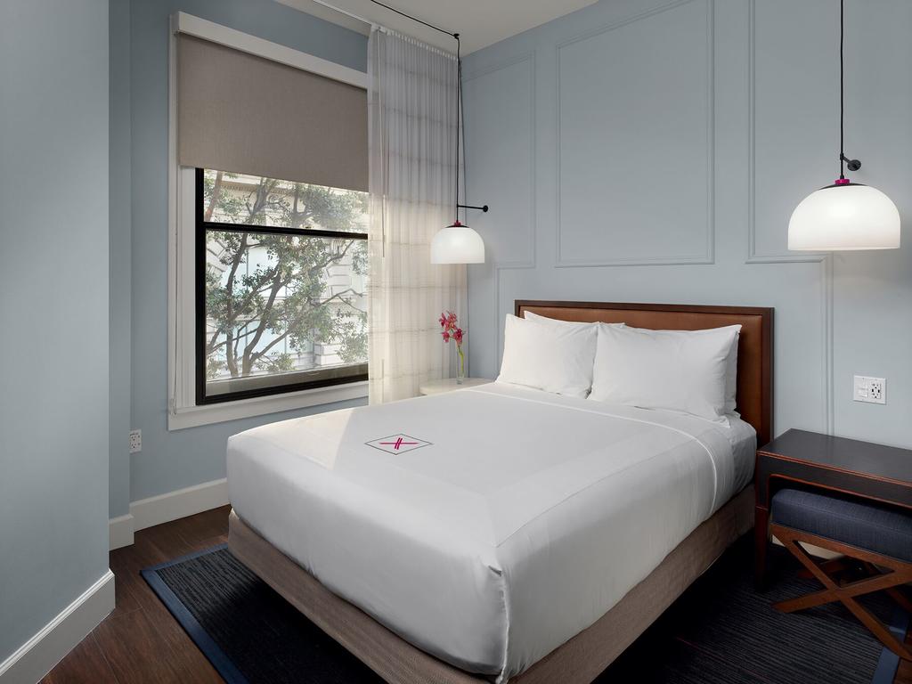 Photo of guest room at Axiom Hotel located in San Francisco. One of the best places to stay in San Francisco. Features a bed with white linens and a window with a tree outside. 