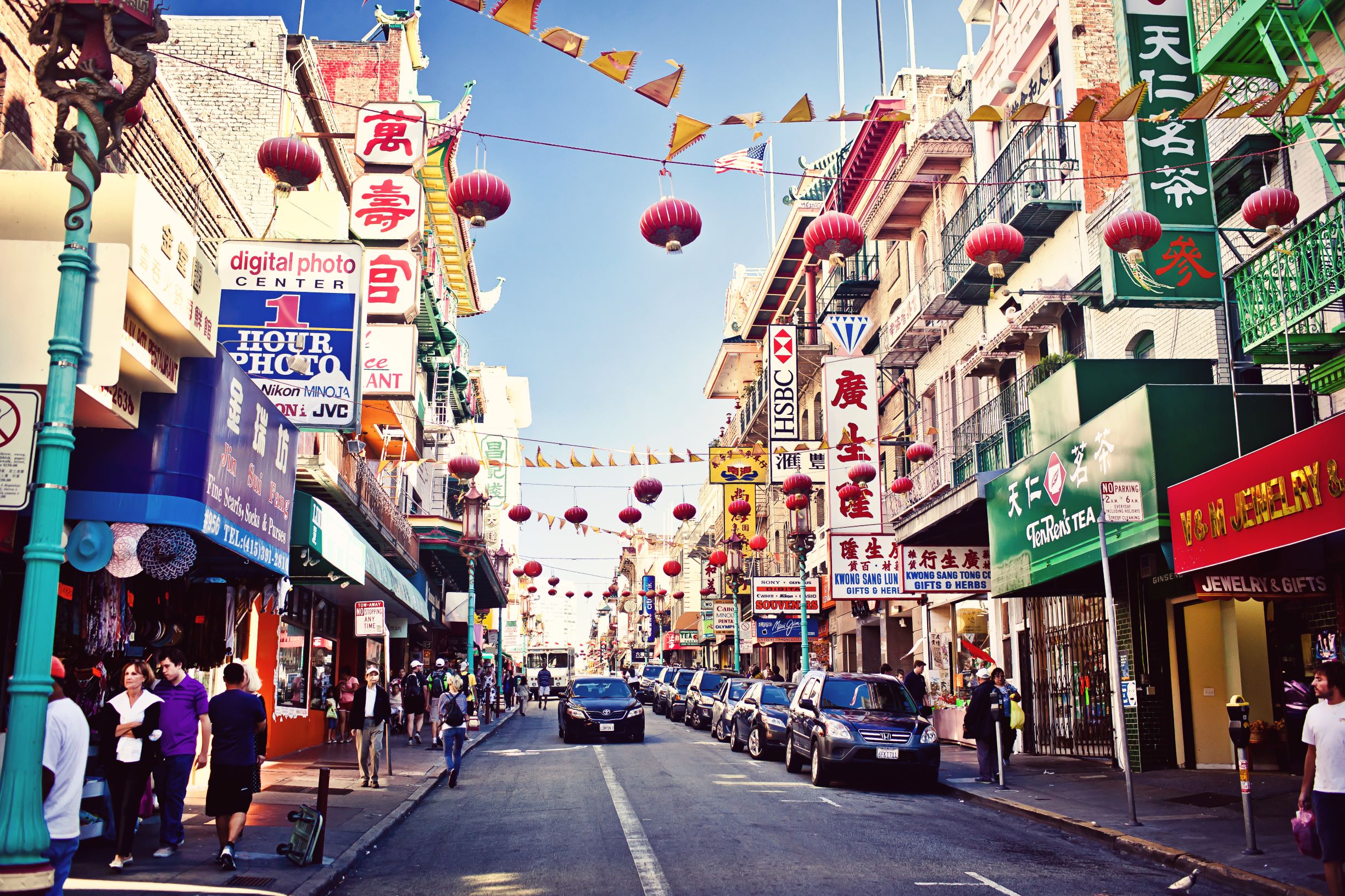 Photo of Chinatown, one of the best places to stay in San Francisco. Photo features a street view of different shops and restaurants with a road in the middle. Lanterns are strung above the street. 