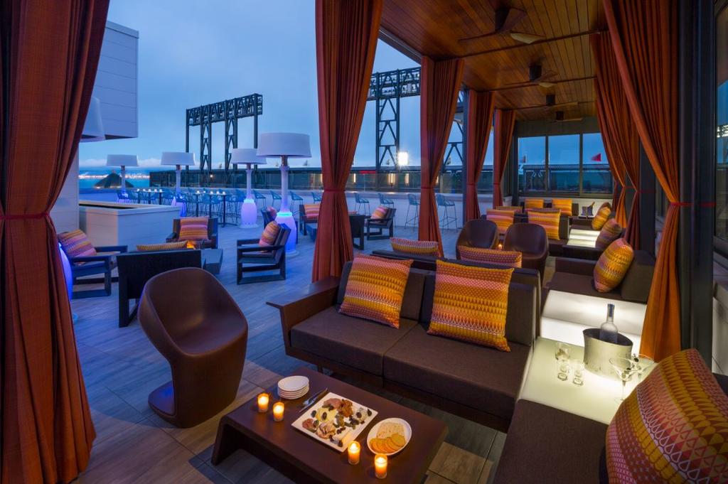 Photo of roof-top bar at Hotel Via in San Francisco. If you are looking for luxury, Hotel Via is one of the best places to stay in San Francisco. Photo features roof-top seating areas with canopy. City skyline is seen in the background.