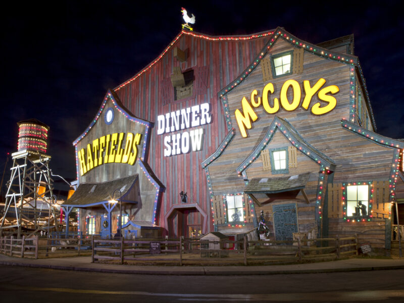 The entrance to the Hatfields and McCoys Dinner Feud in Pigeon Forge. The building looks like an old barn with lights strung across it. 