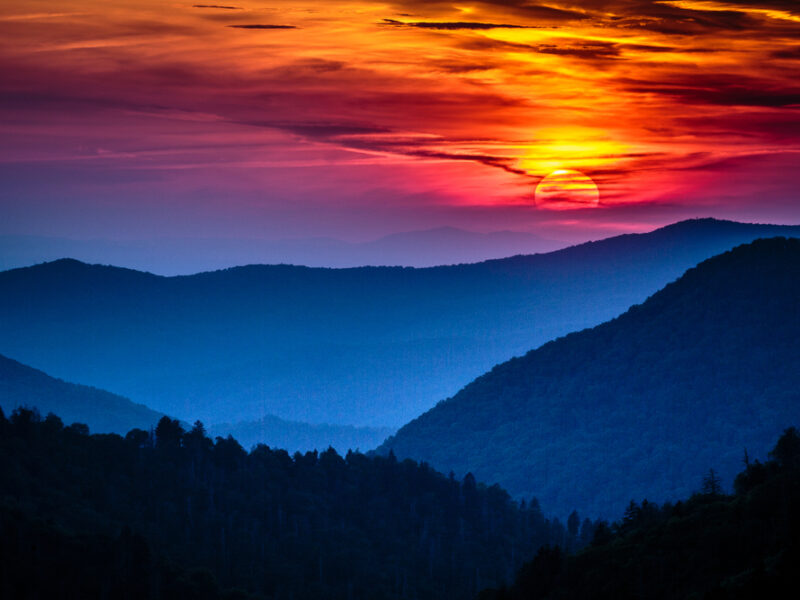 A orange and lilac sunset descends over silhouetted trees in the Smoky Mountains.