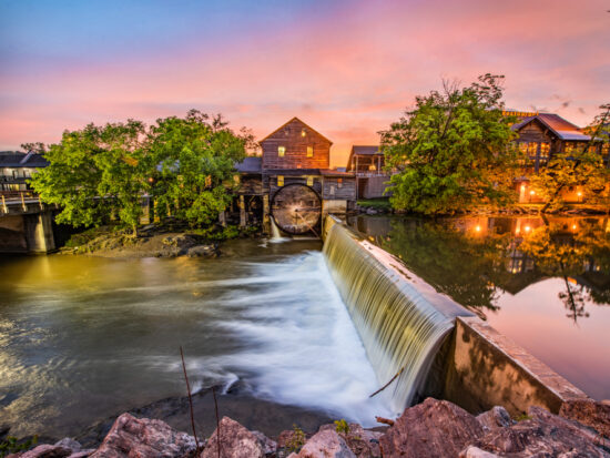 Dusk at the Old Mill, a quaint rustic building next to a small river and overflowing dam.