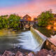 Dusk at the Old Mill, a quaint rustic building next to a small river and overflowing dam.