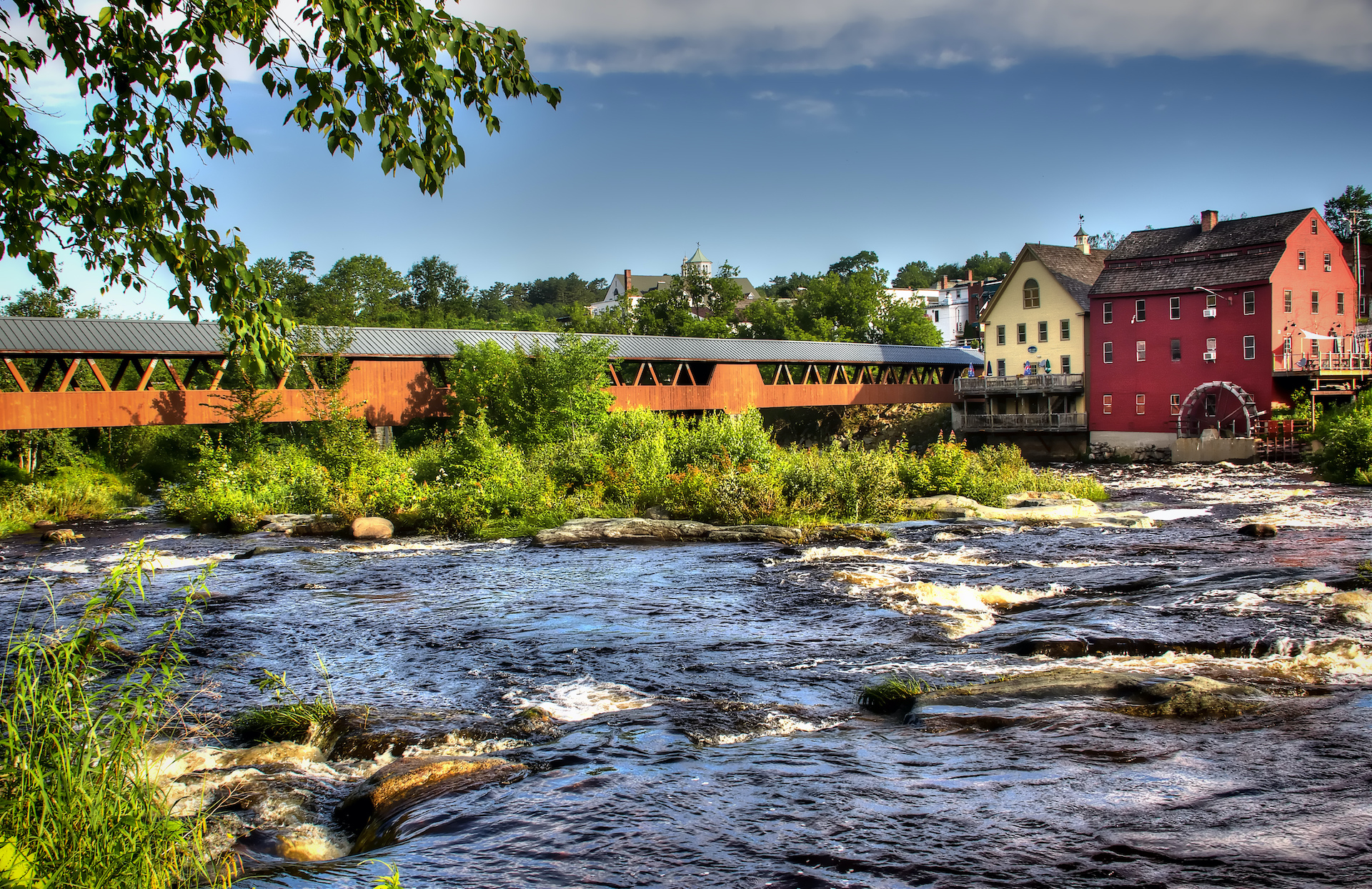 tall red and yellow buildings near red bridge over rushing river