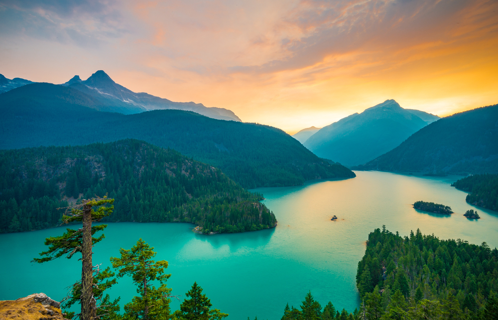 View looking down at the green Lake Diablo nestled among rolling mountains at sunset.