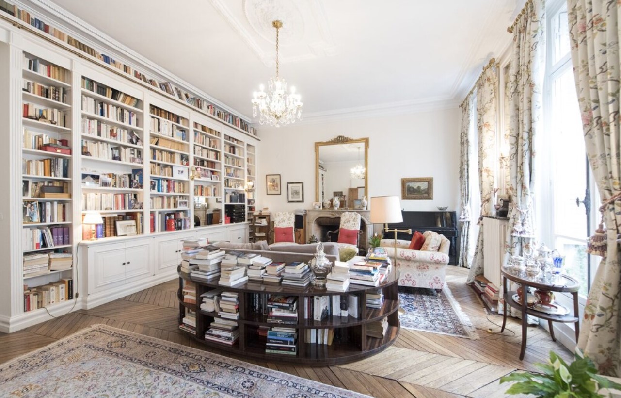 a charming parisian flat with antique mirrors, large windows, a large bookshelf, and cozy couches.