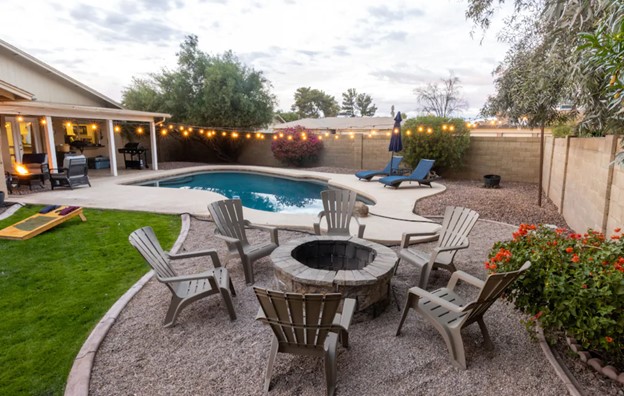 a large backyard with a large pool, string lights, a fire pit with adirondak chairs around it, and pool loungers airbnbs in arizona