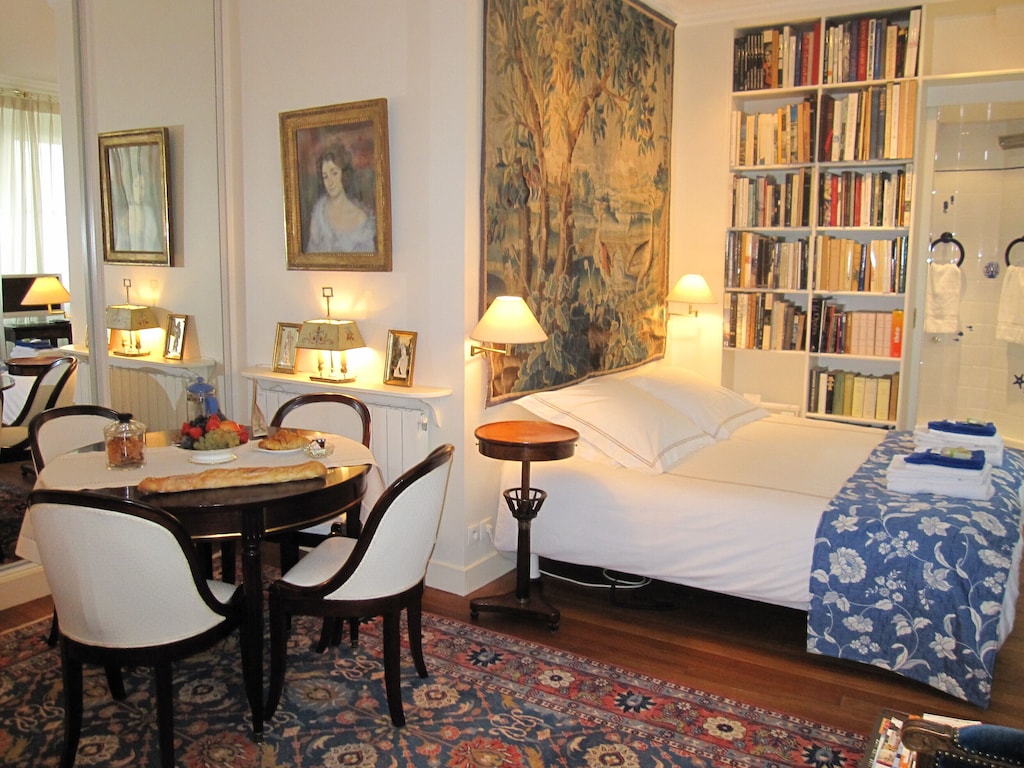 view of the bed, artsy tapestry, and dining table of this studio near the louvre 