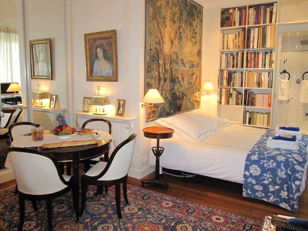 view of the bed, artsy tapestry, and dining table of this studio near the louvre