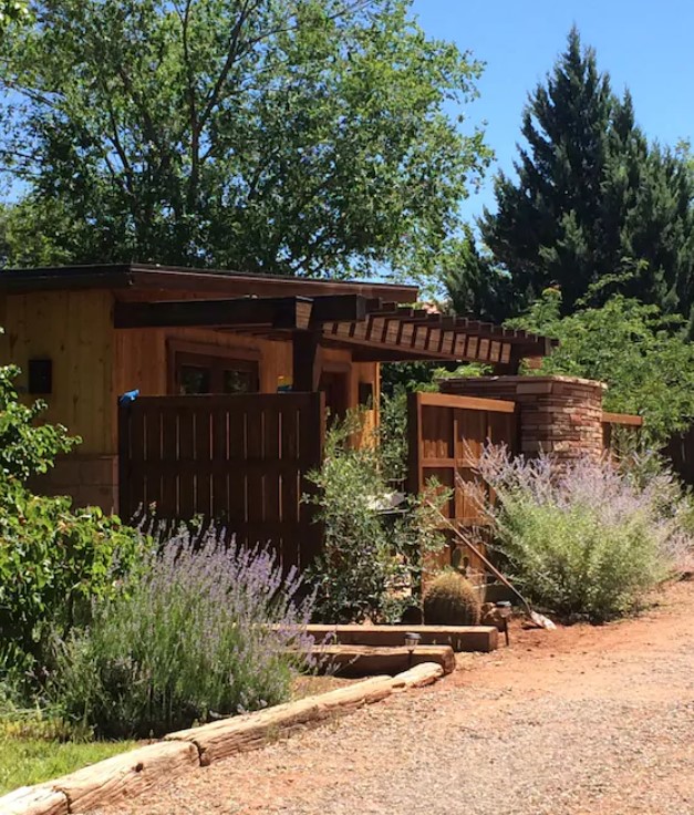 the exterior of a casita in arizona that is surround by lush vegetation, desert land, and large trees on a sunny day