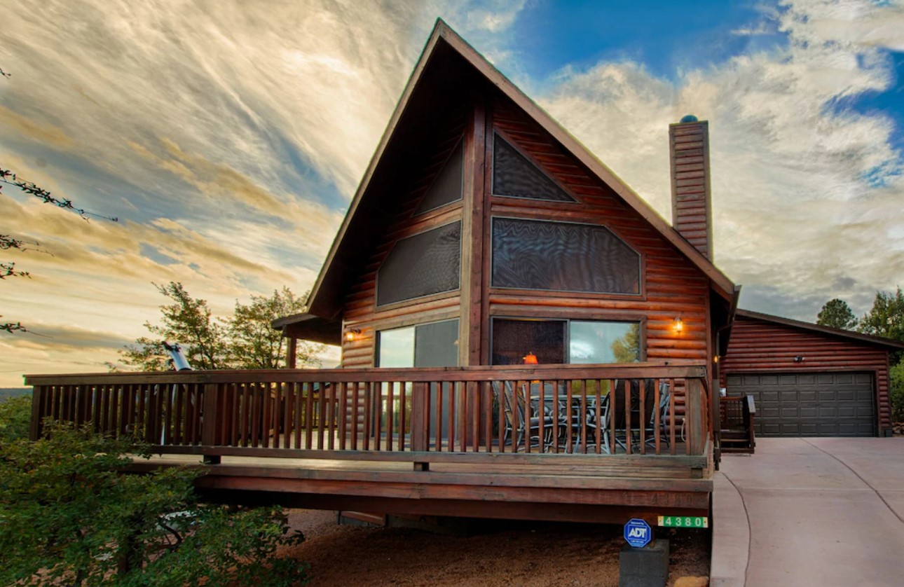 A large log a-frame cabin with a large front deck, floor to ceiling windows, and a garage on the side of it at sunset one of the best airbnbs in Arizona