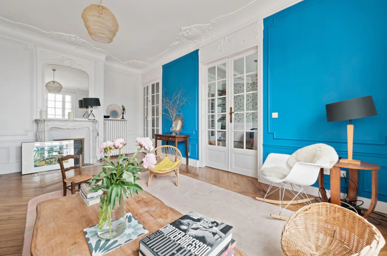 a stylish flat in Paris with a bright blue wall, simple decor, and large windows. 