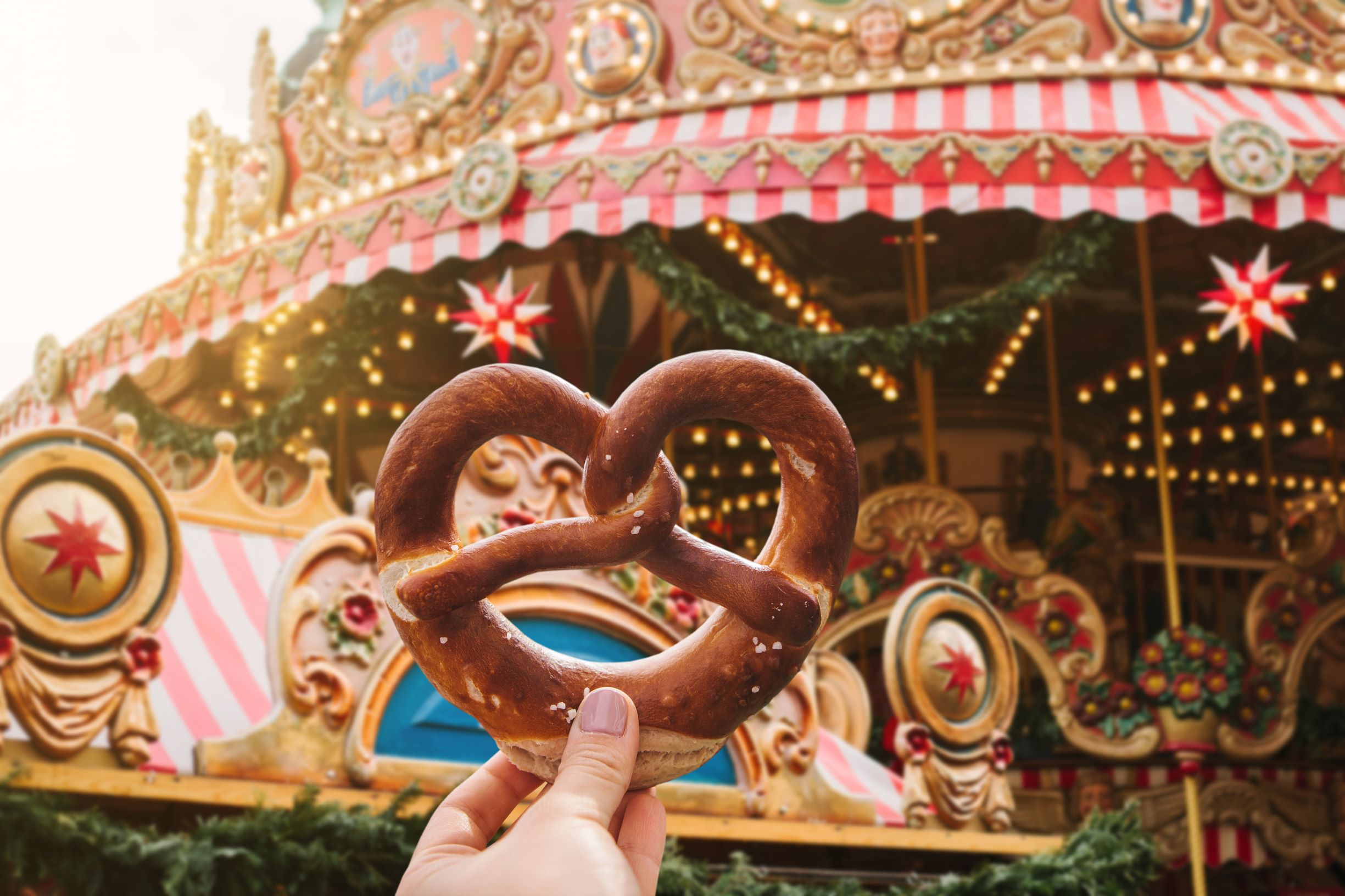 Photo of a large Bavarian pretzel with a Christmas Carousel in the background.