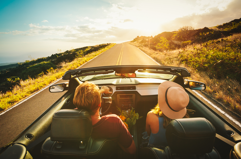 Two friends drive down a road with their hands up