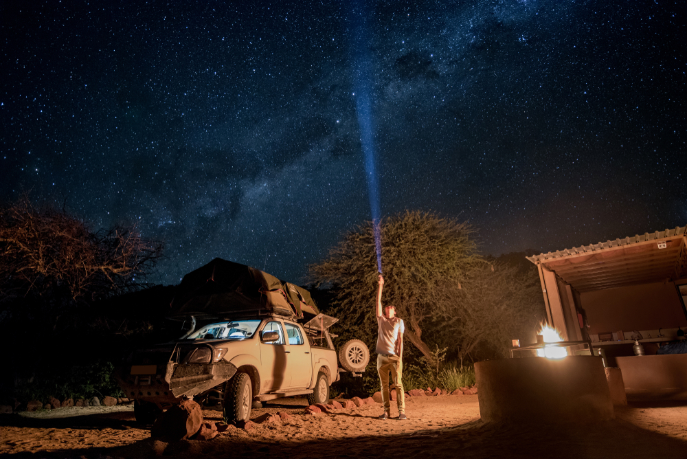 A man flashes a flashlight into the night sky while camping