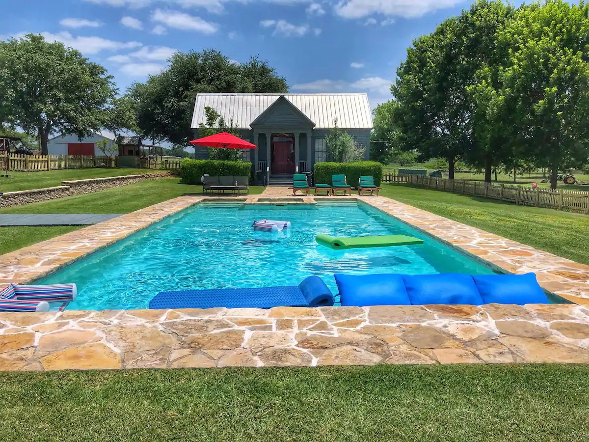 Photo of the exterior of a farmhouse Airbnb that has a pool. 