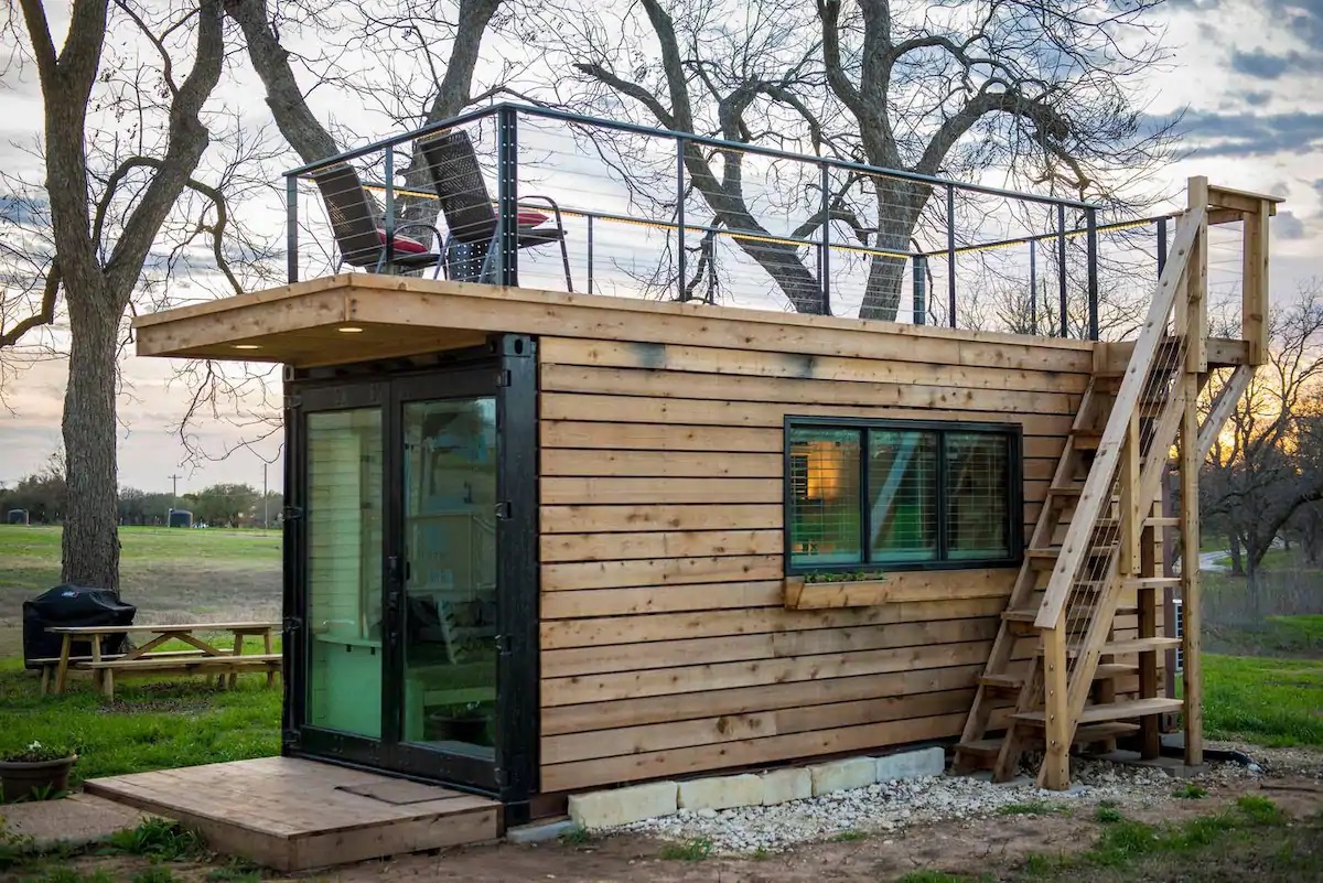 Photo of the exterior of The Stillwater House VRBO located in Waco. It is a small but stylish rectangular tiny home with a rooftop deck. 