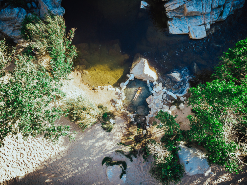 Overhead shot of Deep Creek Hot Springs, a natural California hot springs, with a woman floating in it
