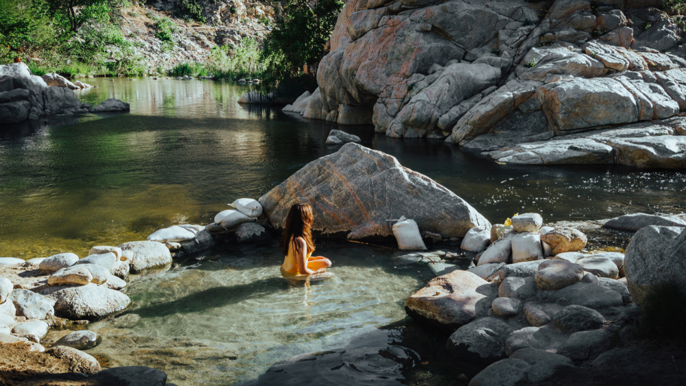 One of the best natural hot springs in California, Deep Creek Hot Springs, with a woman sitting in the middle of the warm water